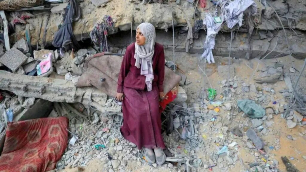 A displaced Palestinian woman sits among the rubble in Gaza during the 2025 ceasefire humanitarian crisis.